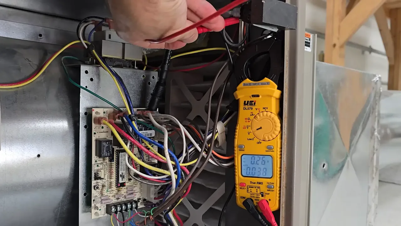 Yellow clamp meter taking an electrical reading beside a furnace control board, with the display showing 0.26 amps