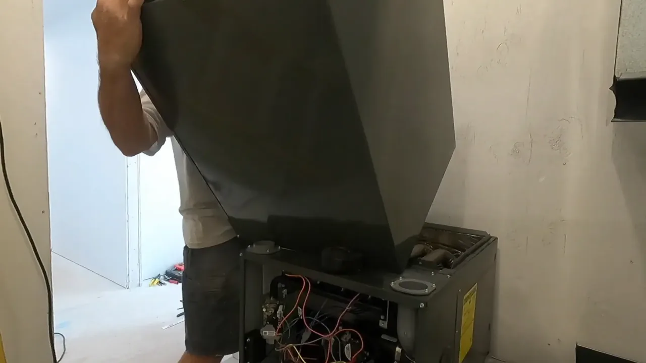 Technician lifting a large dark panel off the top of a furnace, with the burner compartment and wiring exposed below