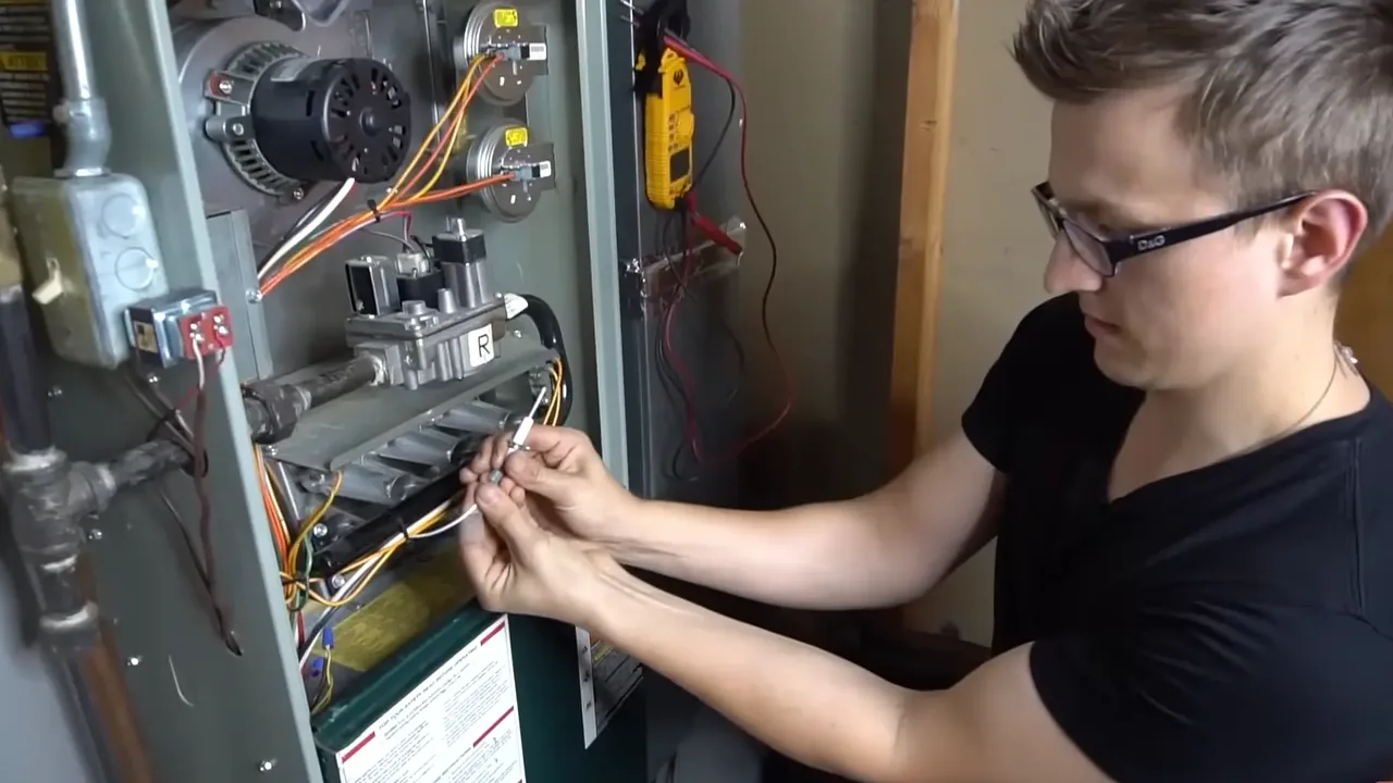 Technician holding a furnace igniter taken from the burner assembly of an open furnace